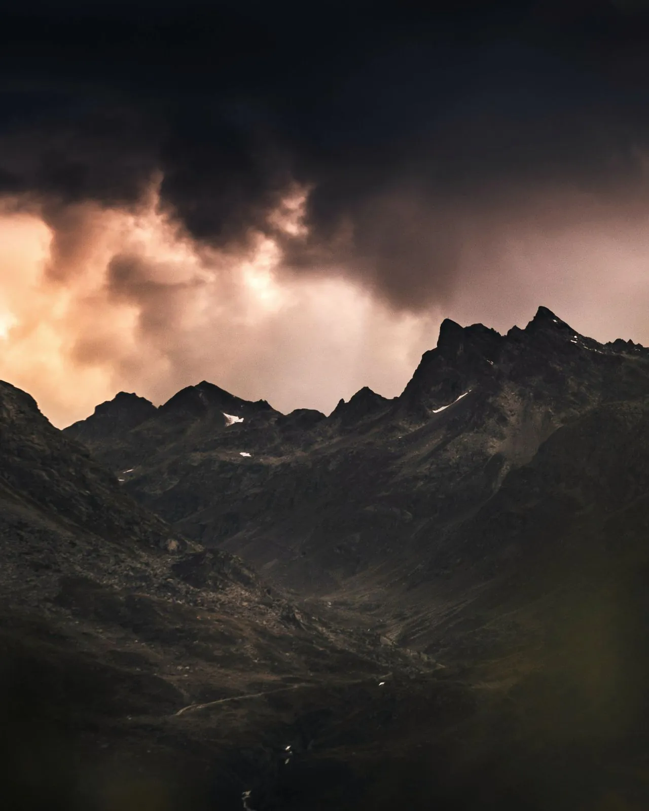 Dark mountain range under a stormy sky lit with copper tones